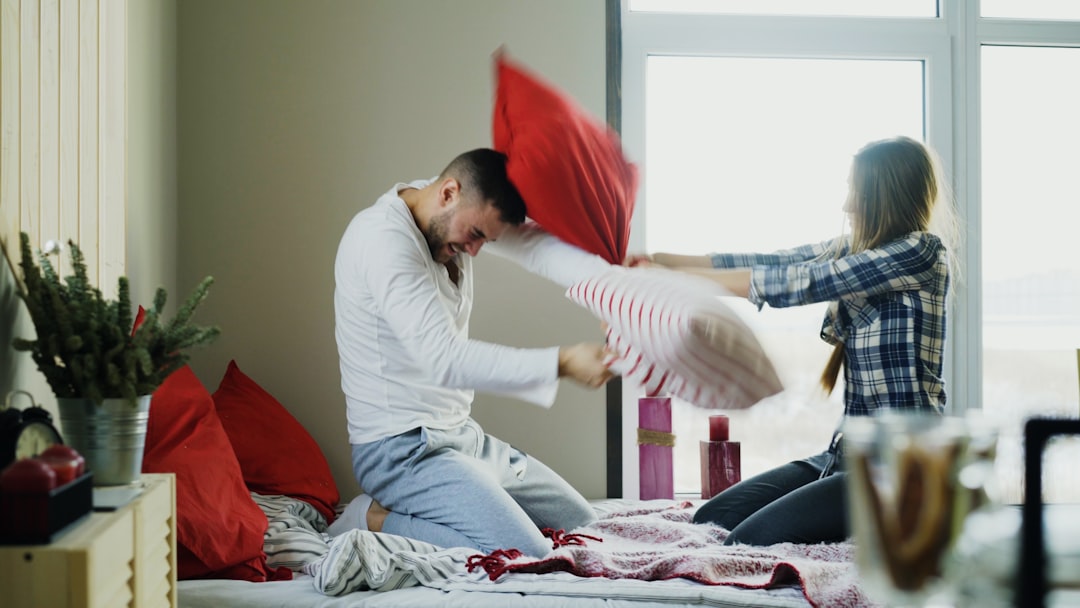 happy and loving couple fight pillows in bed at home in the morning