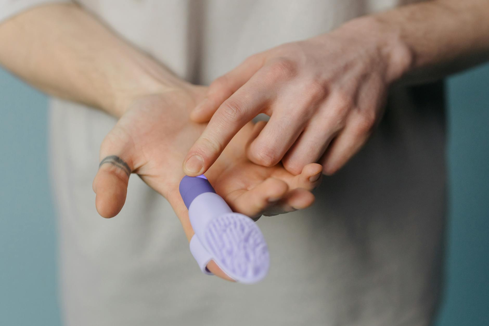 An adult hand holding a purple silicone finger massager against a neutral background.
