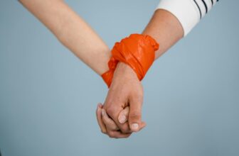 Symbolic close-up of hands tied together with an orange band, highlighting unity or constraint.