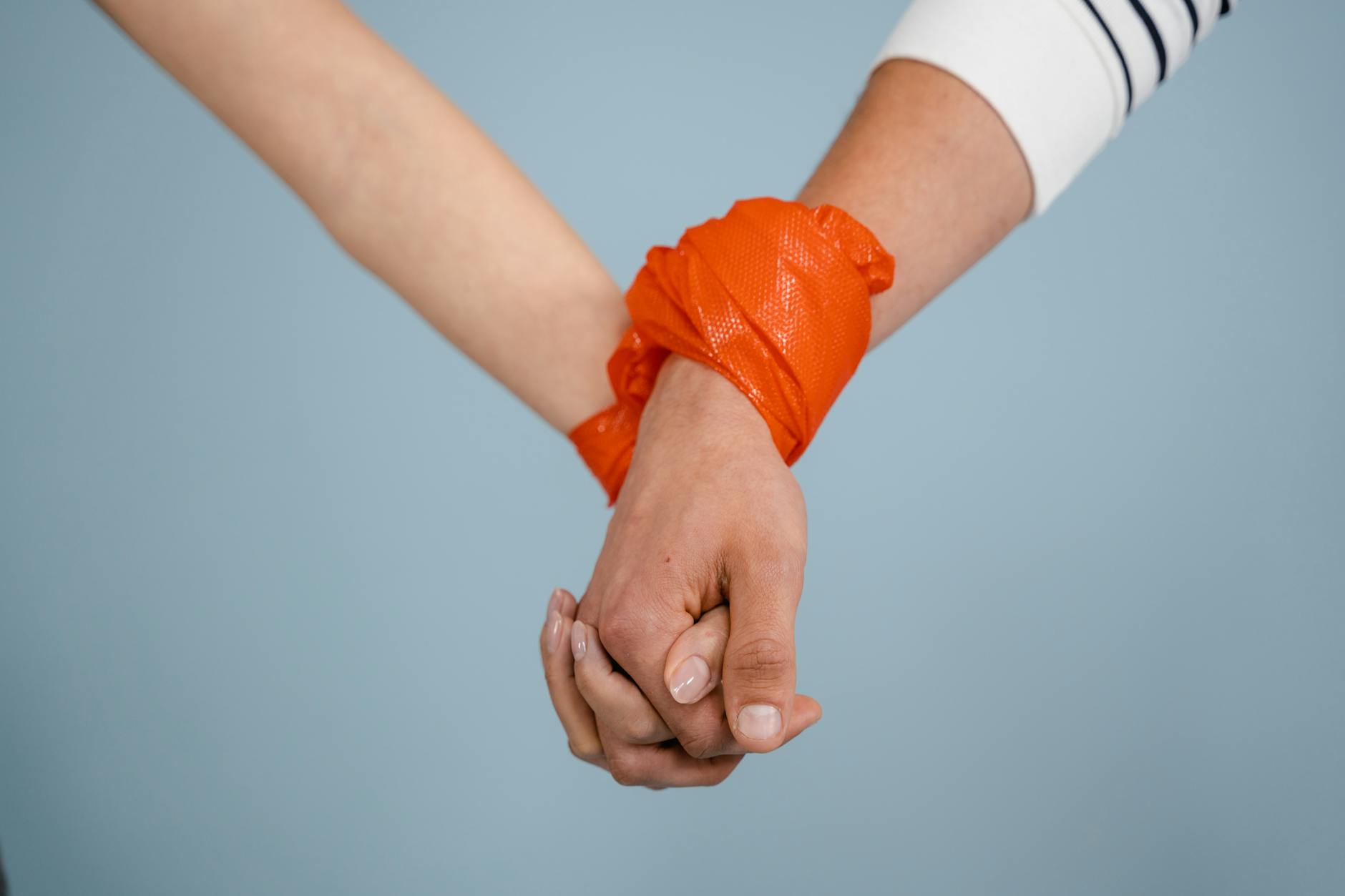 Symbolic close-up of hands tied together with an orange band, highlighting unity or constraint.