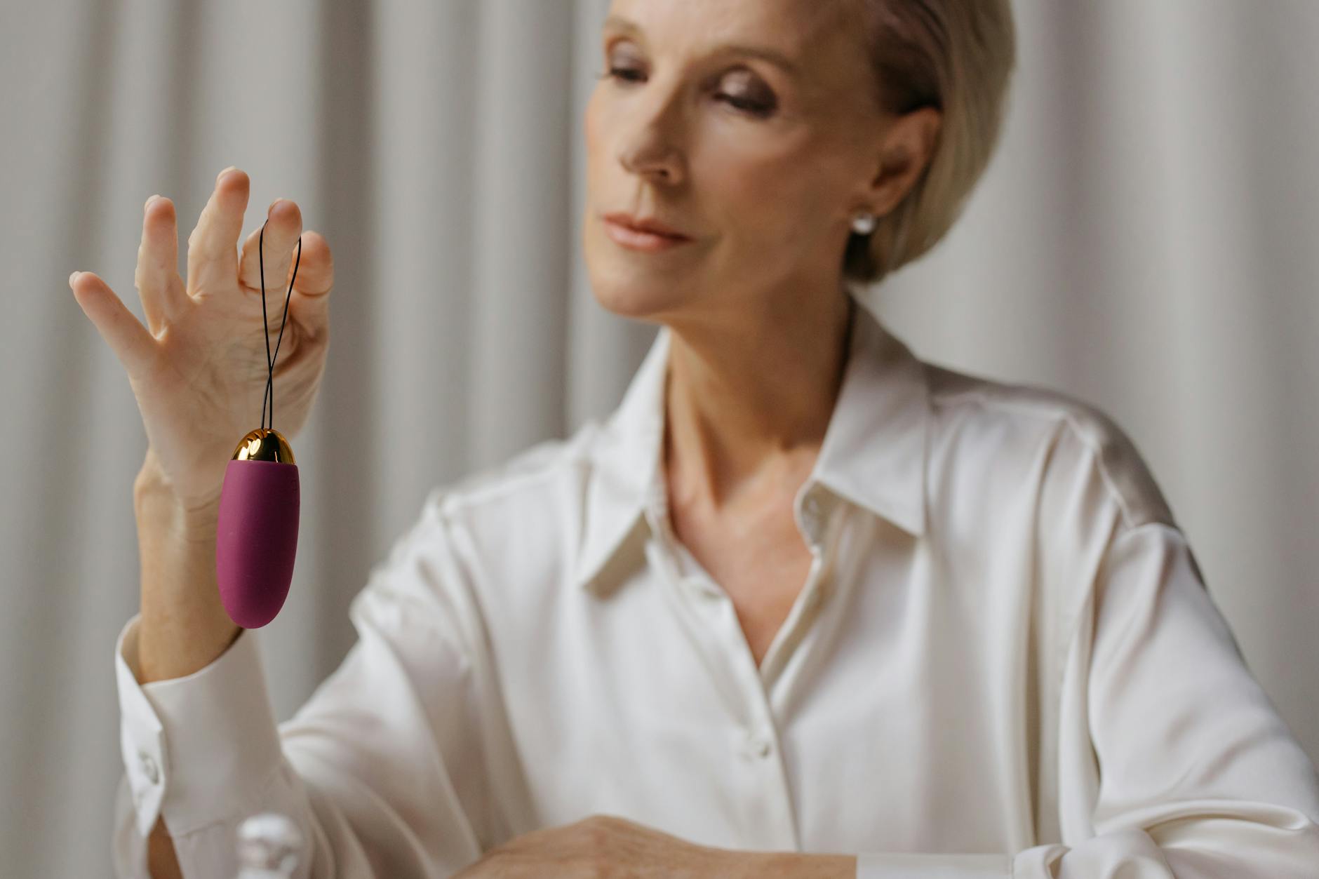 Mature woman in white blouse examining a purple vibrator indoors.