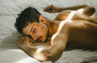 A contemplative young man lying on a bed illuminated by sunbeams, capturing a moment of peace.