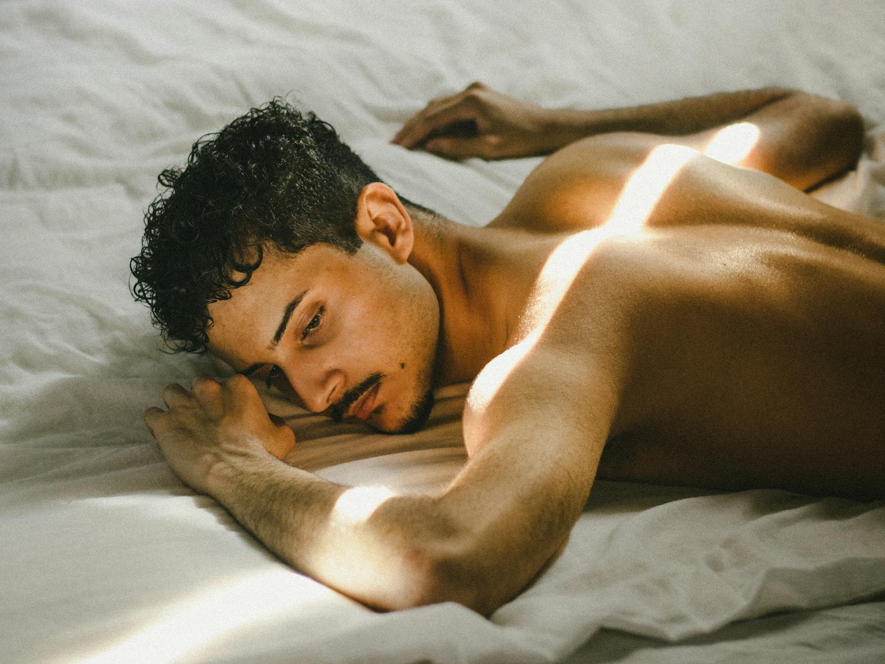 A contemplative young man lying on a bed illuminated by sunbeams, capturing a moment of peace.