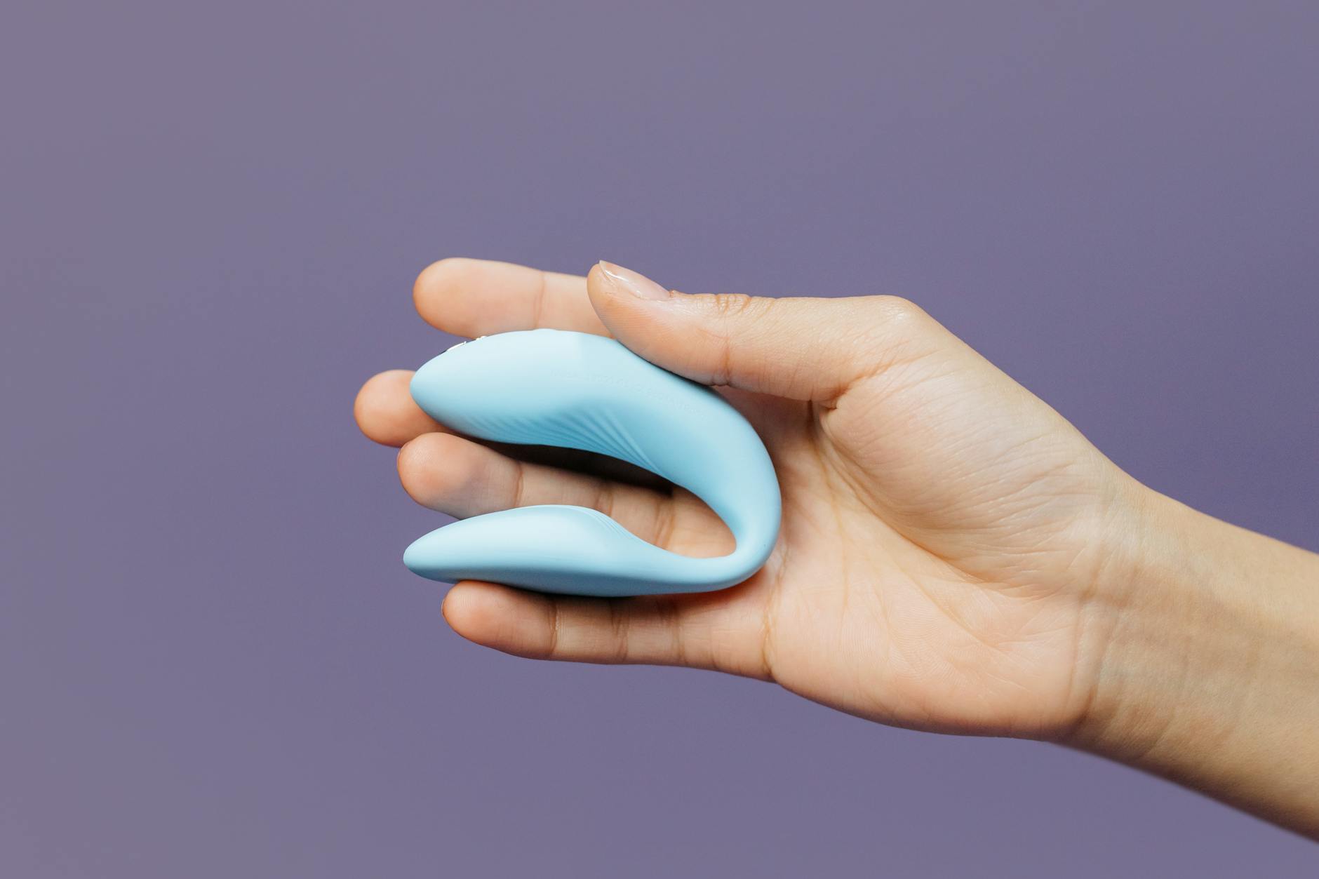 A hand holding a small blue vibrator against a purple background, symbolizing intimacy
