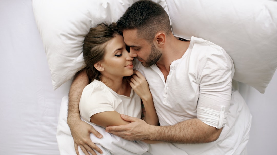 Young beautiful and loving couple kiss and hug into bed while waking up in the morning