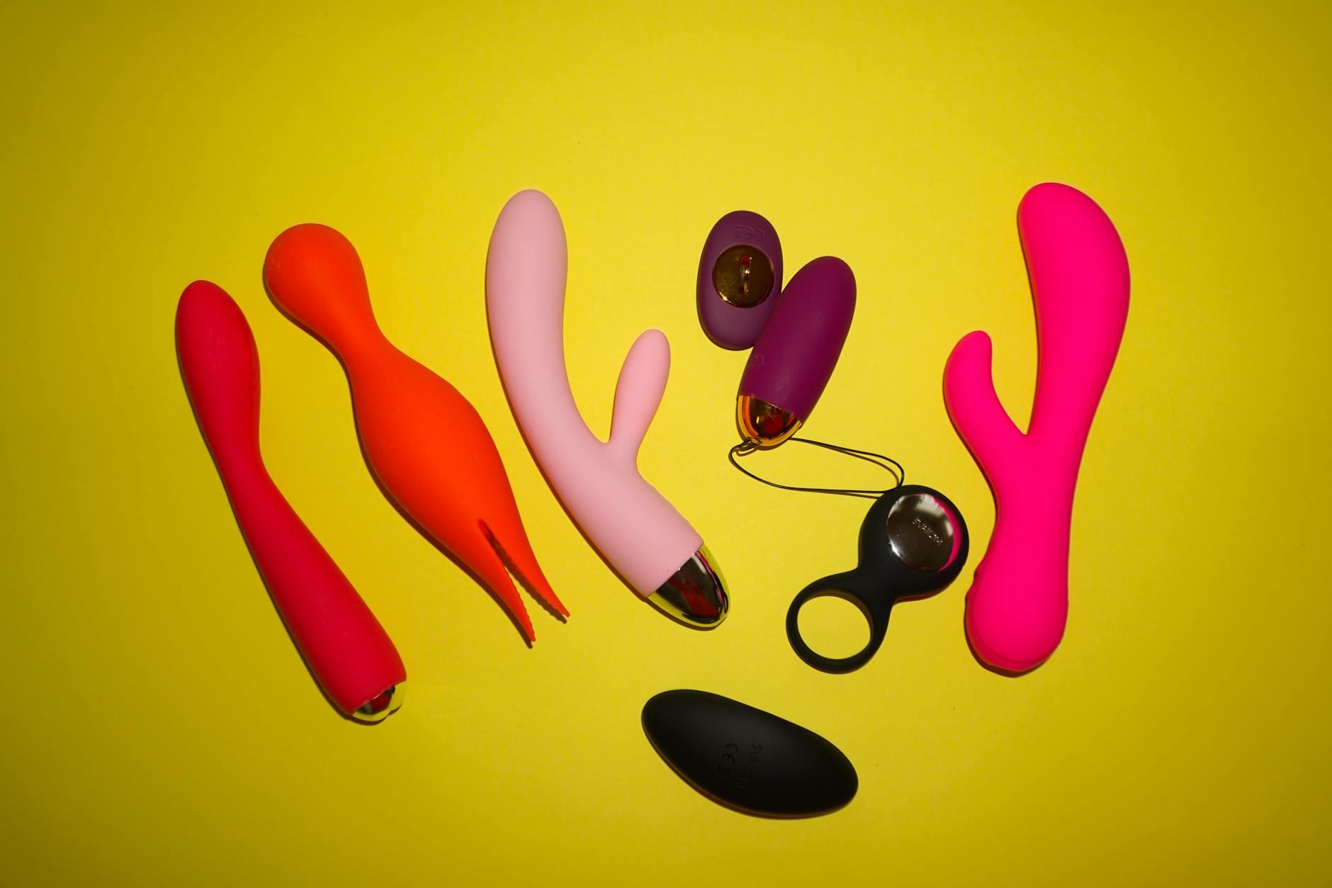 Studio setup showcasing colorful sex toys on a bright yellow background, featuring various shapes and designs