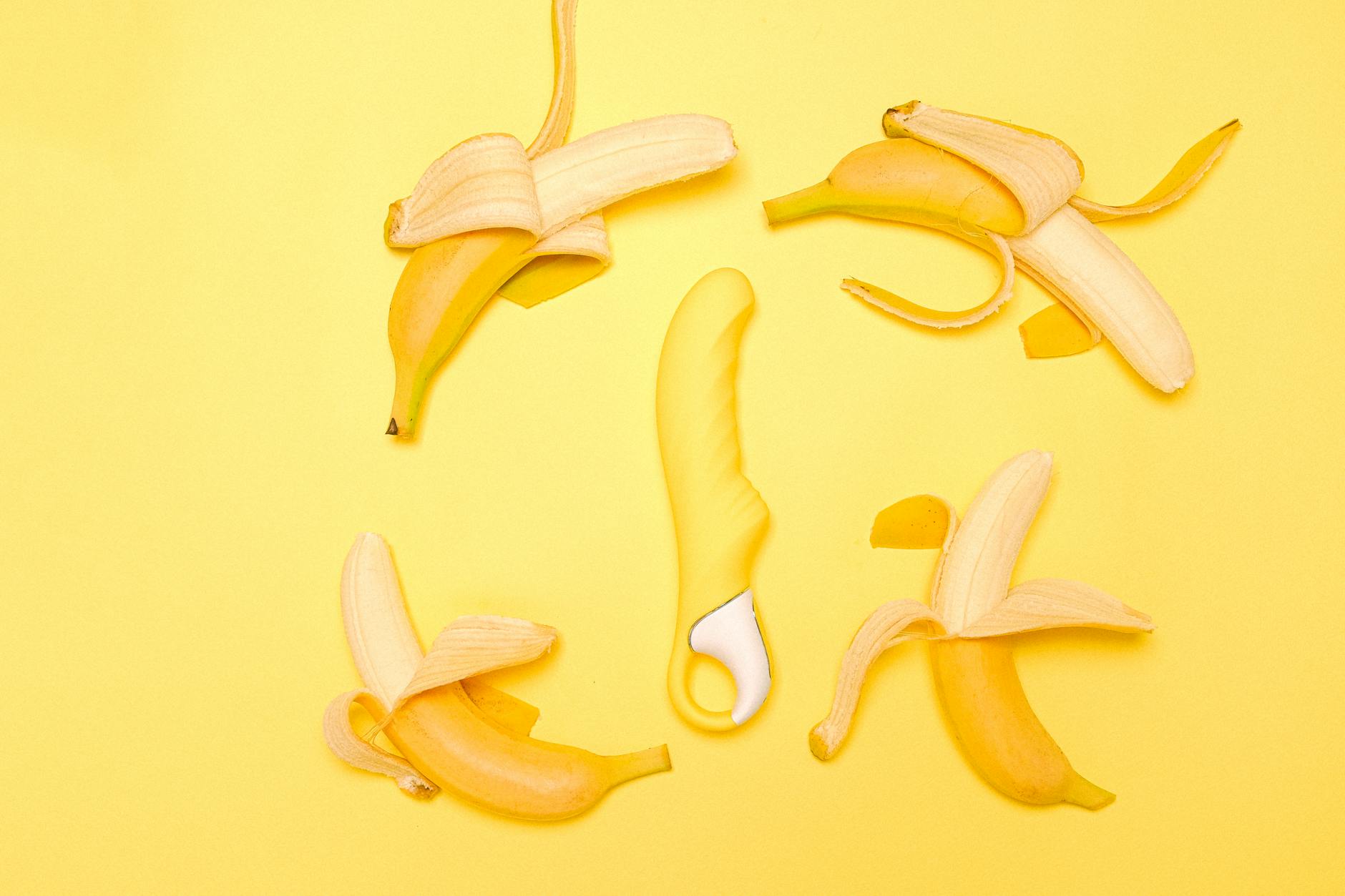 Creative flat lay of a yellow silicone vibrator surrounded by peeled bananas on a yellow background