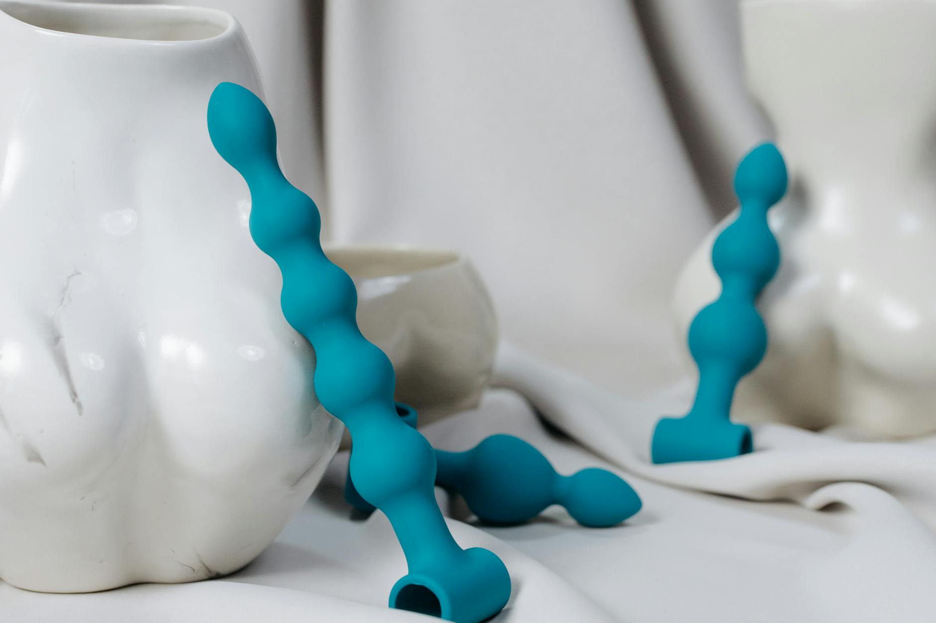 Artistic composition of blue silicone anal beads and vases. Soft lighting enhances the sensual aesthetic