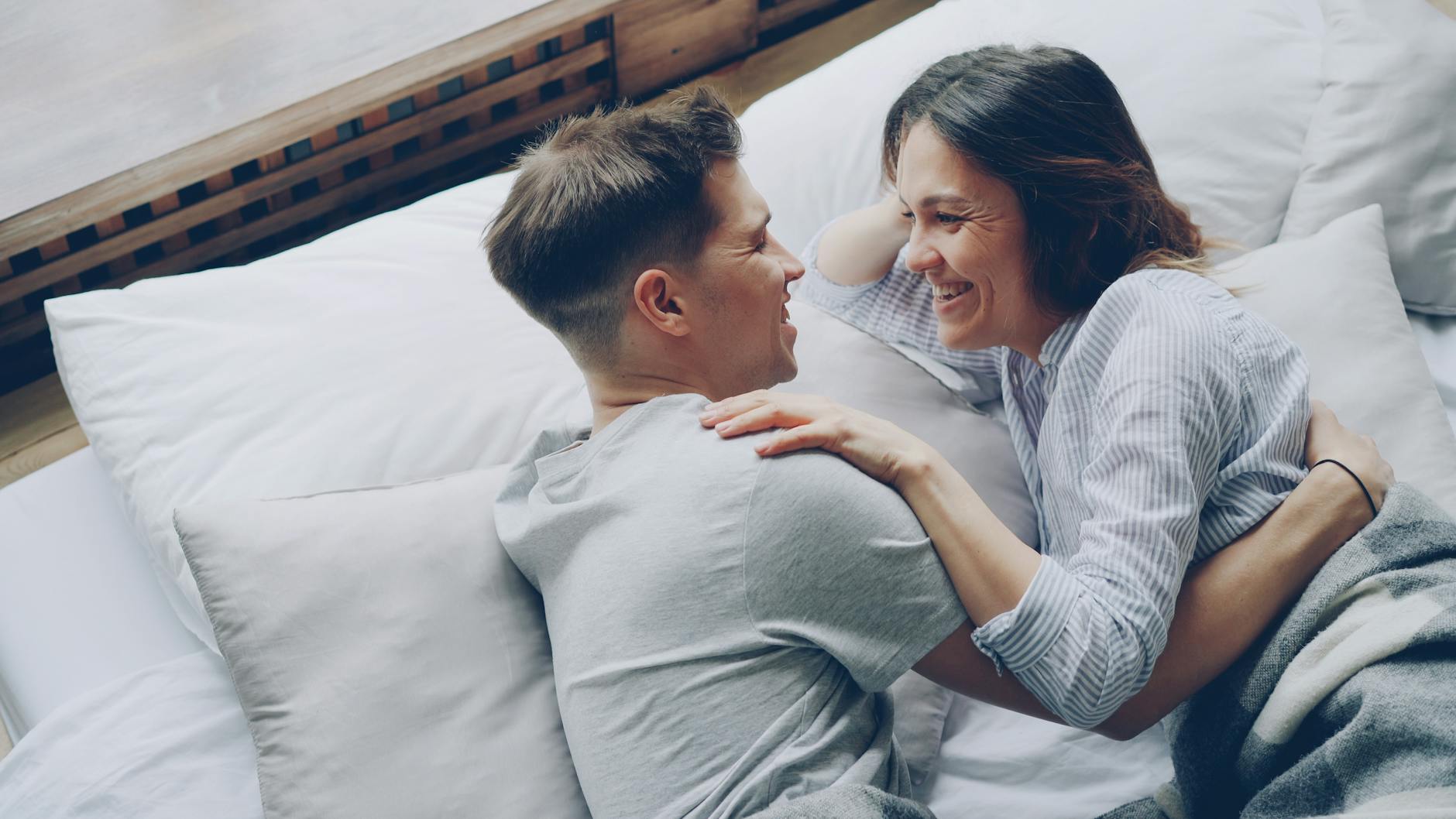 A joyful moment of a couple laughing and embracing on a bed, conveying love and happiness