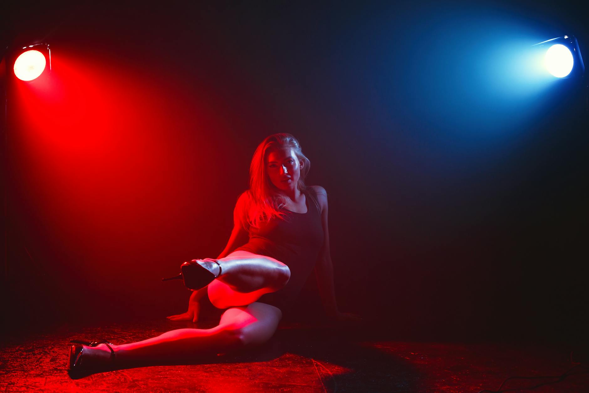 A woman in heels posing under sharp red and blue light, creating a moody, seductive atmosphere.