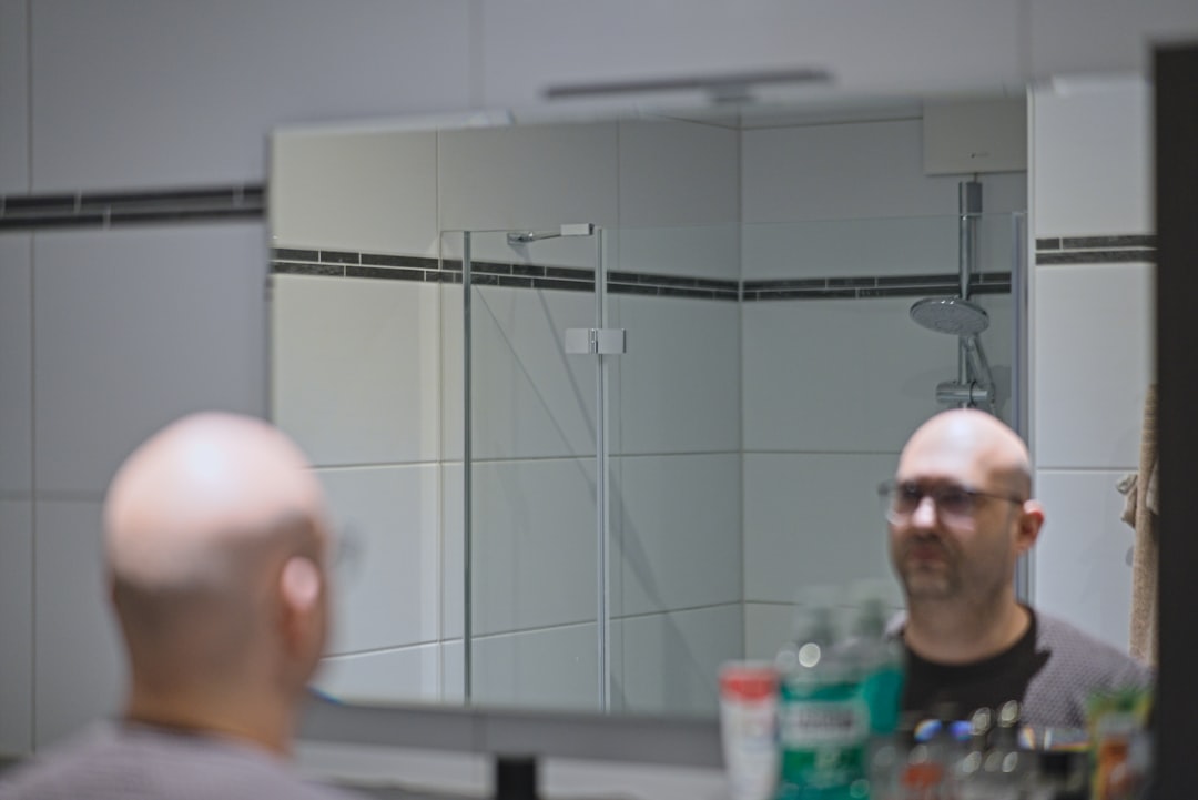 Bald man with glasses looking in bathroom mirror