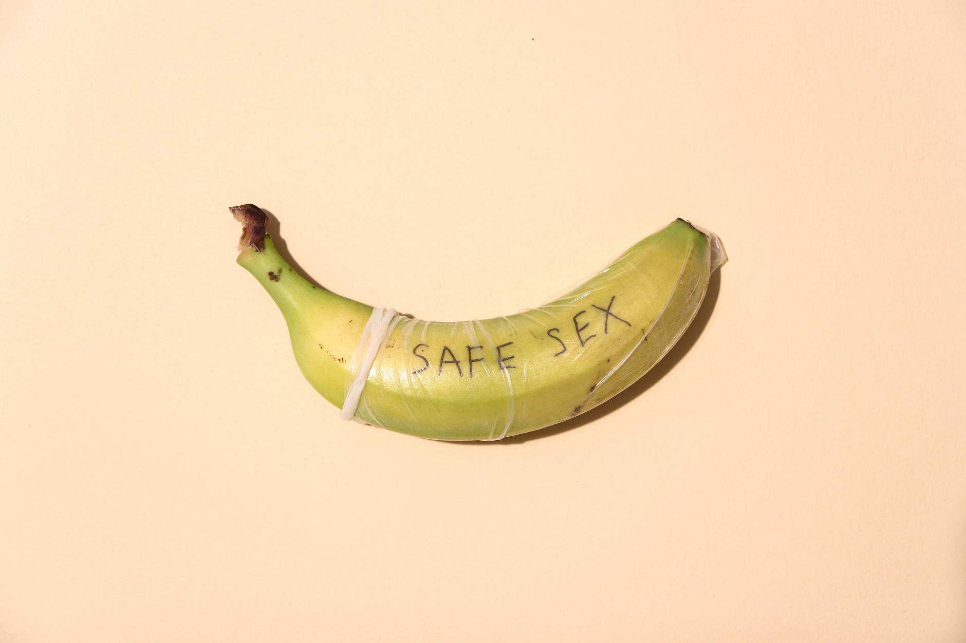 A banana wrapped in a condom for safe sex awareness on a pastel background