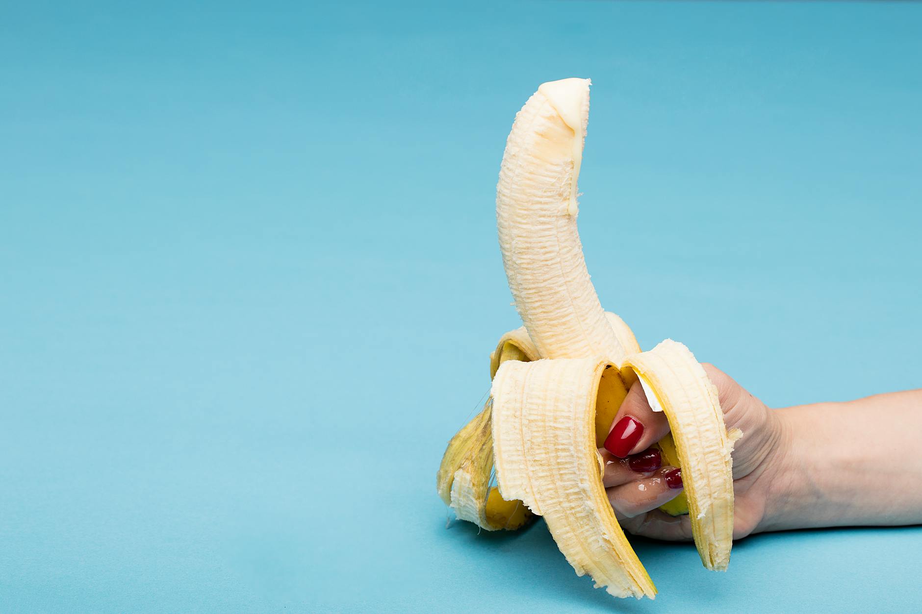 A close-up of a hand holding a peeled banana with a vibrant blue background, composition ideal for food photography