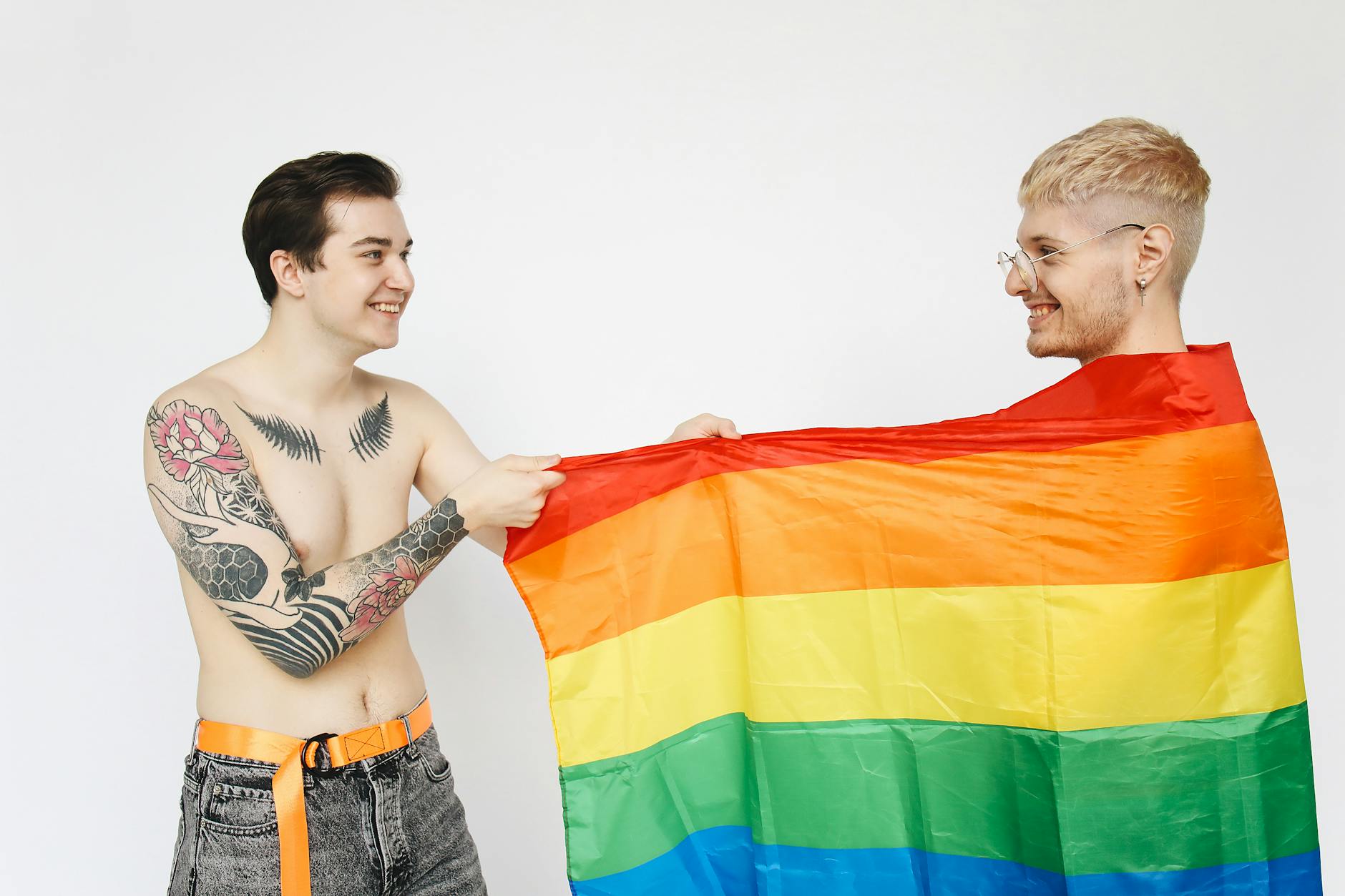 Happy tattooed couple holding a rainbow flag celebrating LGBT pride indoors