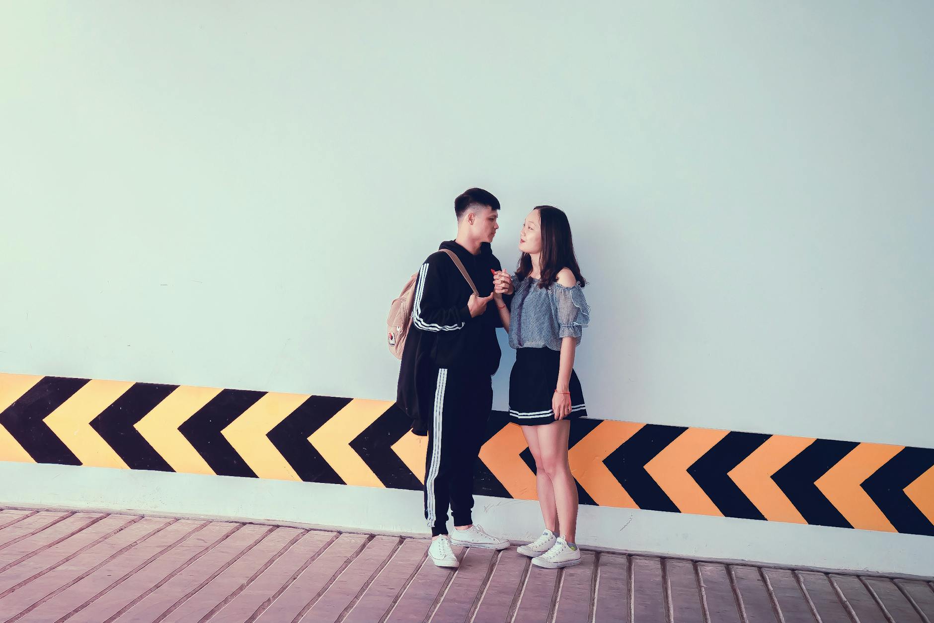 A young couple interacting by a modern wall with diagonal patterns, sharing a moment