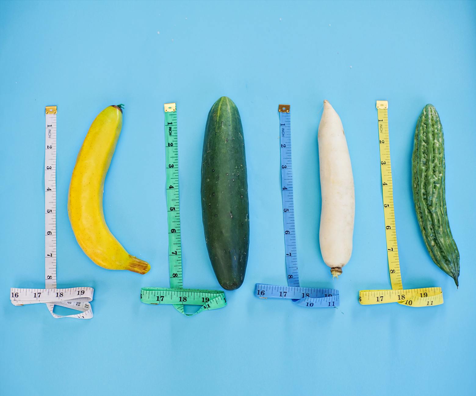 A vibrant still life of various vegetables and measuring tapes on a blue backdrop