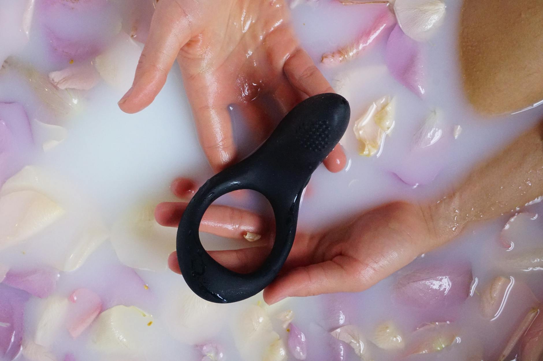 Hands holding a black adult toy in a floral bath, focusing on sensuality and relaxation
